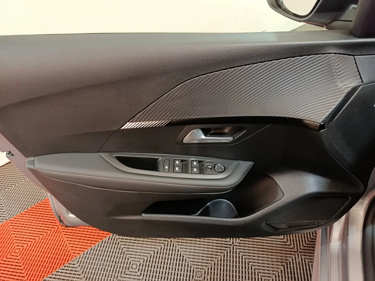 Porte avant gauche de Peugeot 208 gris clair 2025, avec commandes électriques et insert décoratif effet carbone.