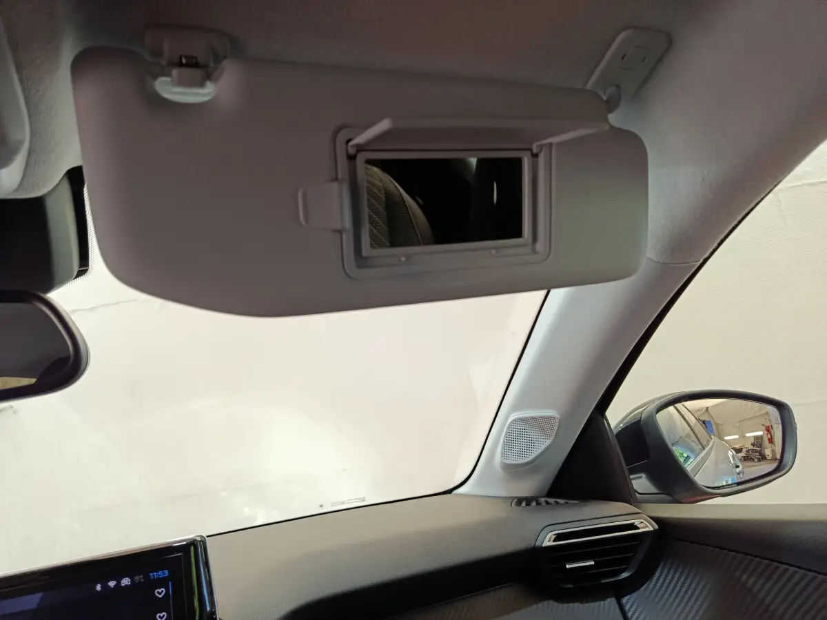 Intérieur de la Peugeot 208 gris clair, vue côté passager avec pare-soleil et rétroviseur extérieur visible.