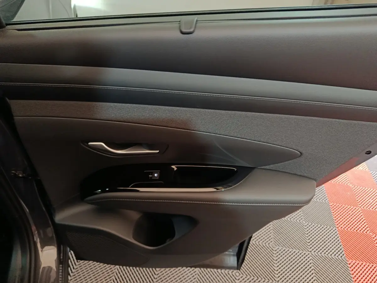 Vue intérieure du panneau de porte côté conducteur gris foncé avec commandes de fenêtre et poignée argentée sur Hyundai Tucson 2025.