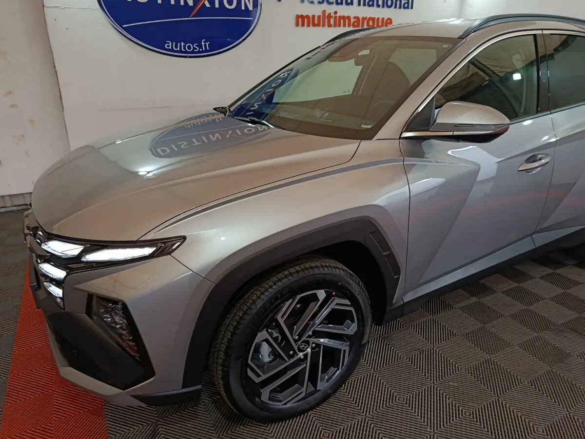 Vue 3/4 avant droit d'un Hyundai Tucson gris clair avec phares LED et jantes alliage au design géométrique.