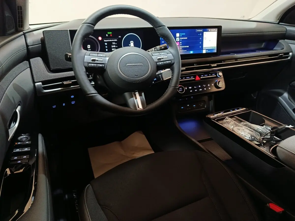 Intérieur noir du Hyundai Tucson 1.6 Hybrid 2025 vu côté conducteur, avec tableau de bord numérique et écran tactile central.