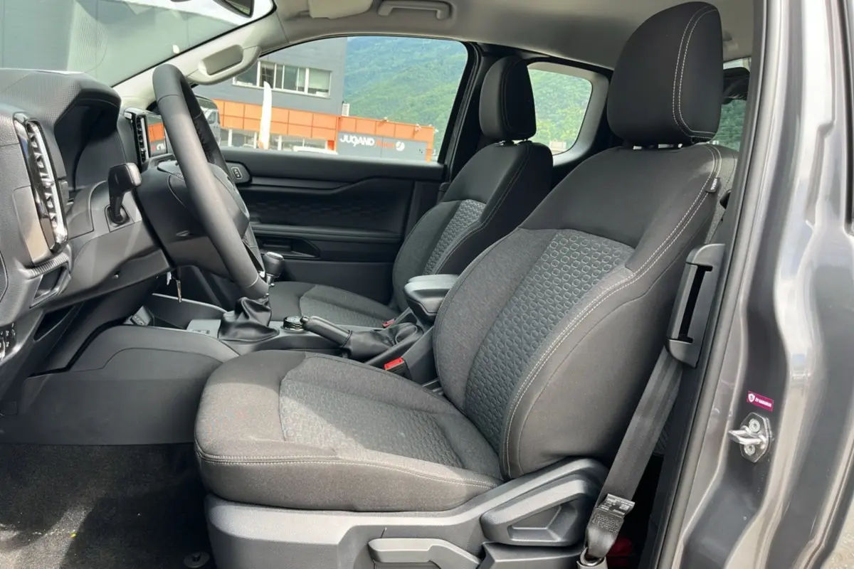 Vue intérieure côté conducteur du Ford Ranger gris carbone 2025, sièges tissu avec accoudoir central et volant multifonctions.