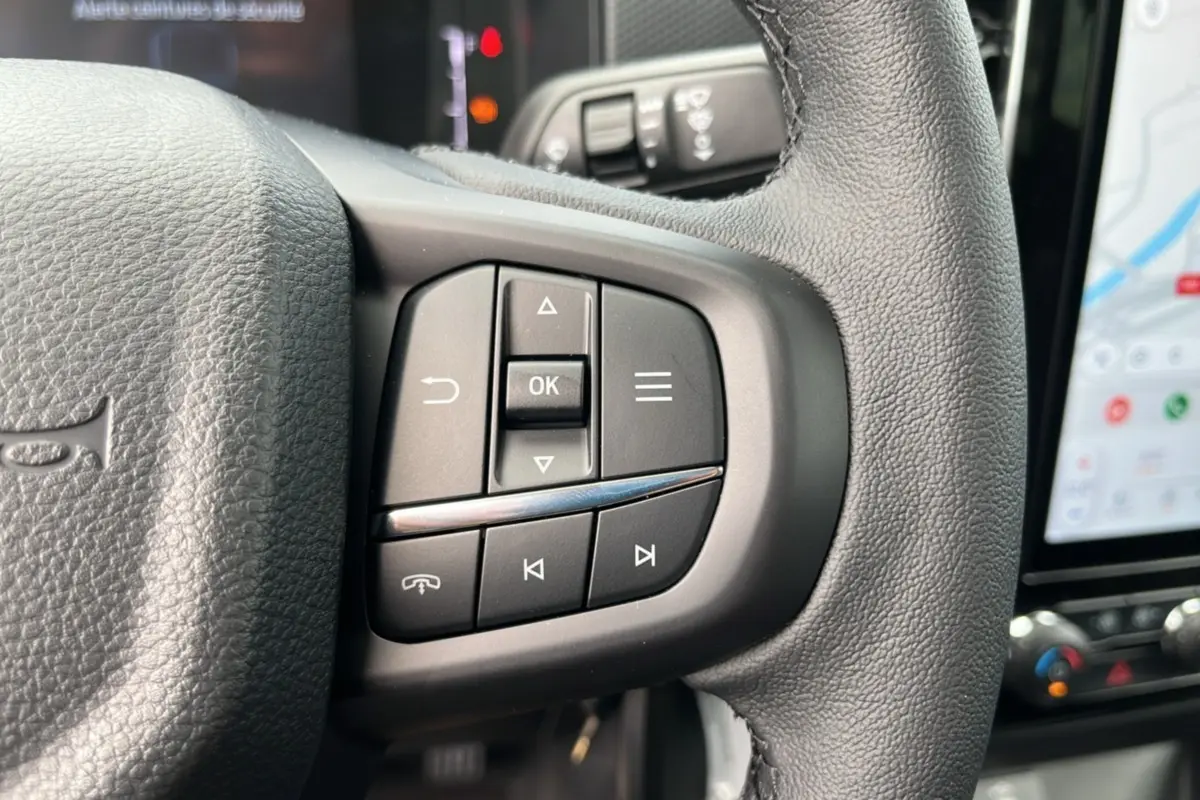 Gros plan sur les commandes multifonctions du volant cuir noir du Ford Ranger 2025 avec écran tactile en arrière-plan.