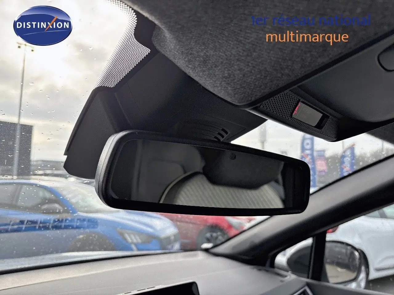 Vue intérieure du rétroviseur central d’un Renault Captur gris rafale métal avec toit noir, sous un ciel nuageux et pluie légère.