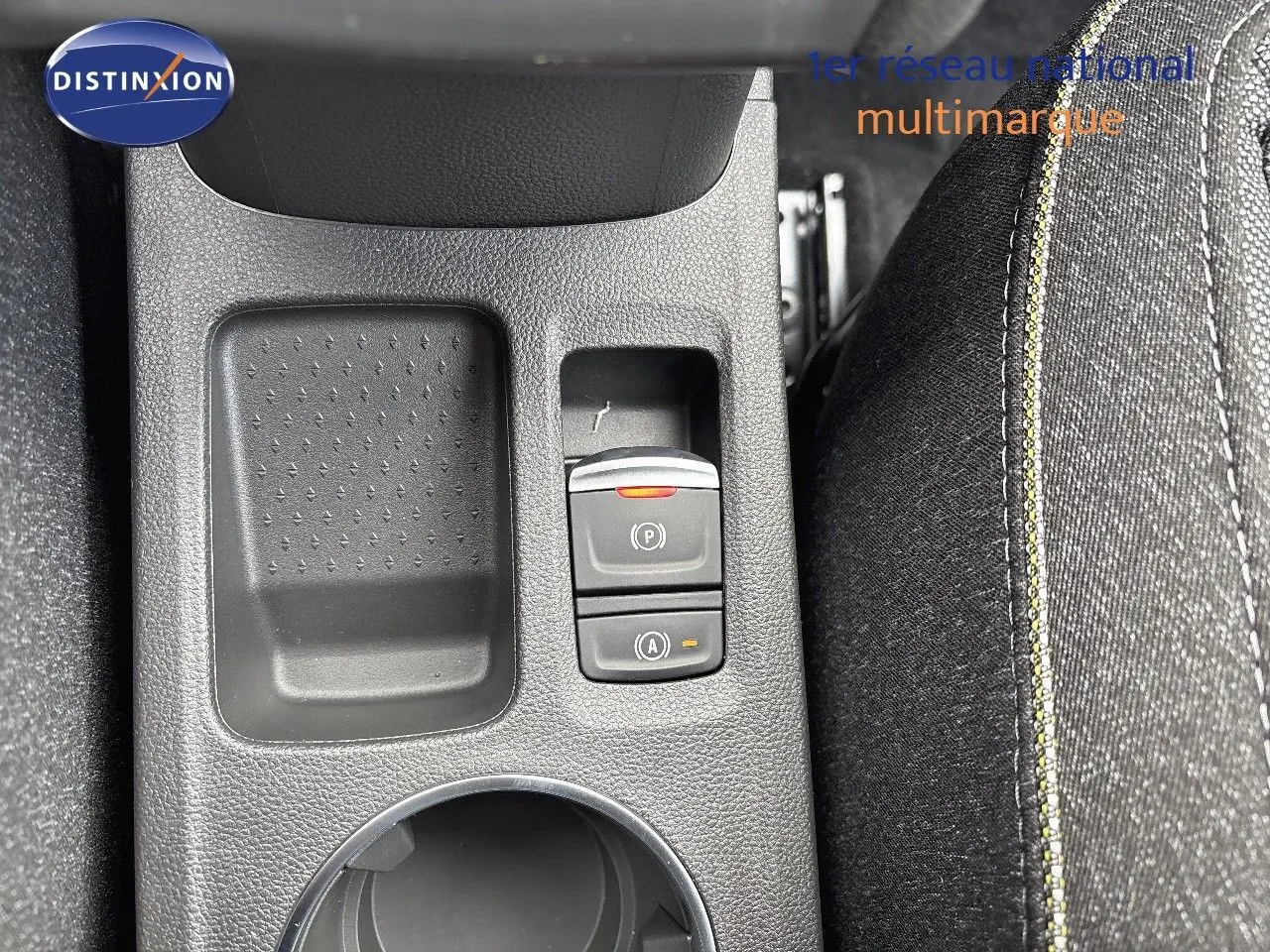 Gros plan sur la console centrale avec les boutons de frein à main électrique et auto hold, tissu noir avec surpiqûres jaunes.