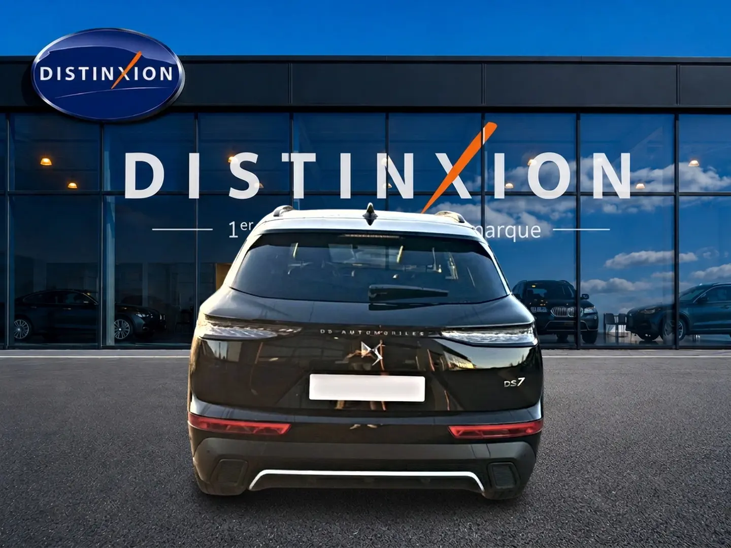 Vue arrière d'un DS7 noir 2026 stationné devant une vitrine avec logo Distinxion visible en reflet.