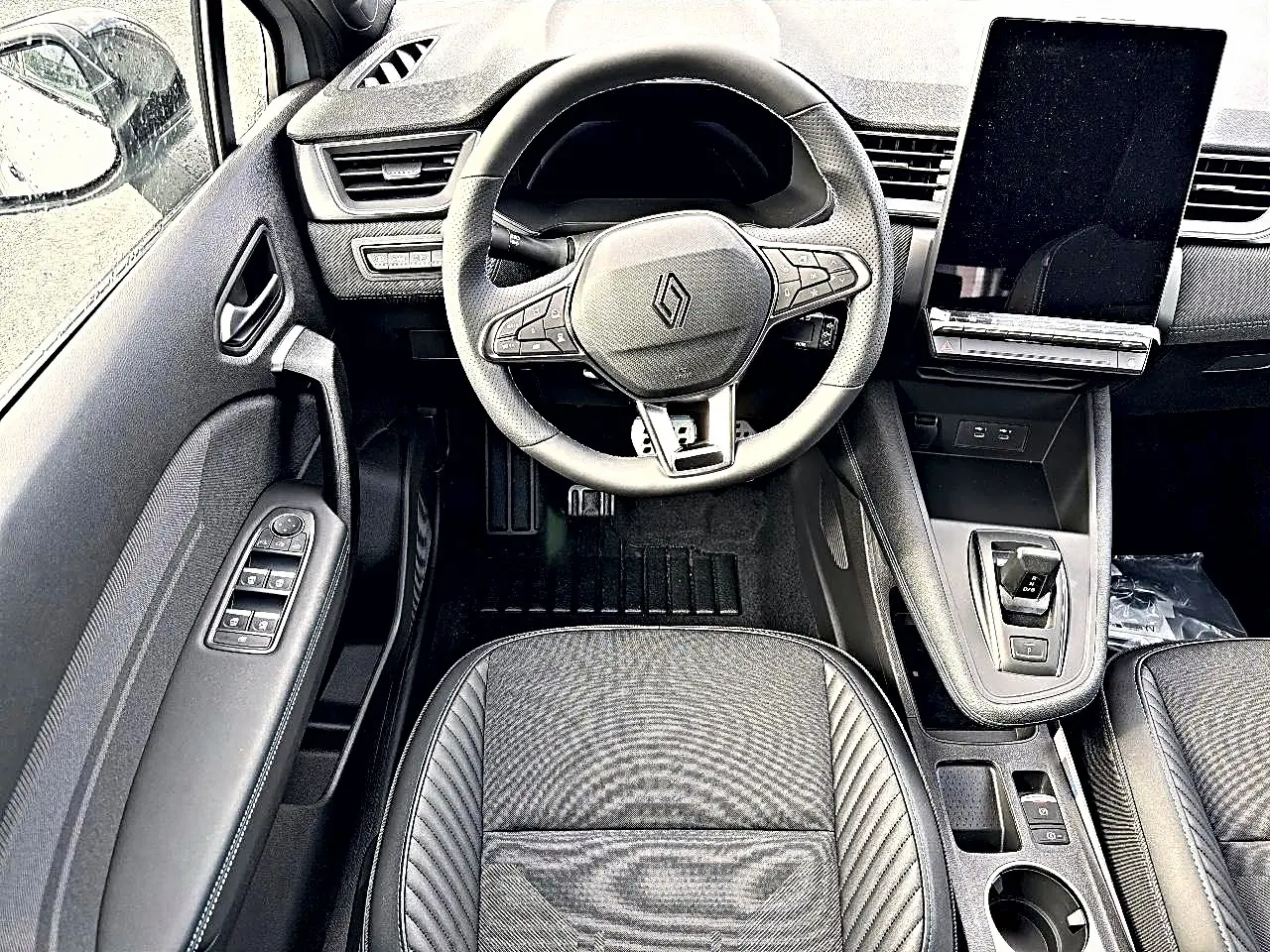 Vue intérieure centrée sur le volant et la console centrale du Renault Symbioz gris, avec écran tactile vertical et commandes au volant.