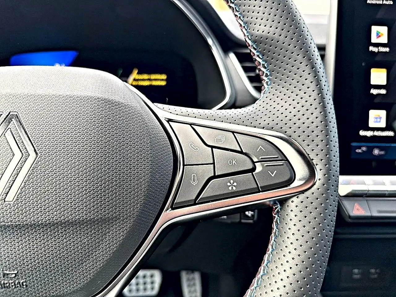 Gros plan sur le volant perforé avec commandes multifonctions du Renault Symbioz gris rafale, tableau de bord et écran tactile visibles.