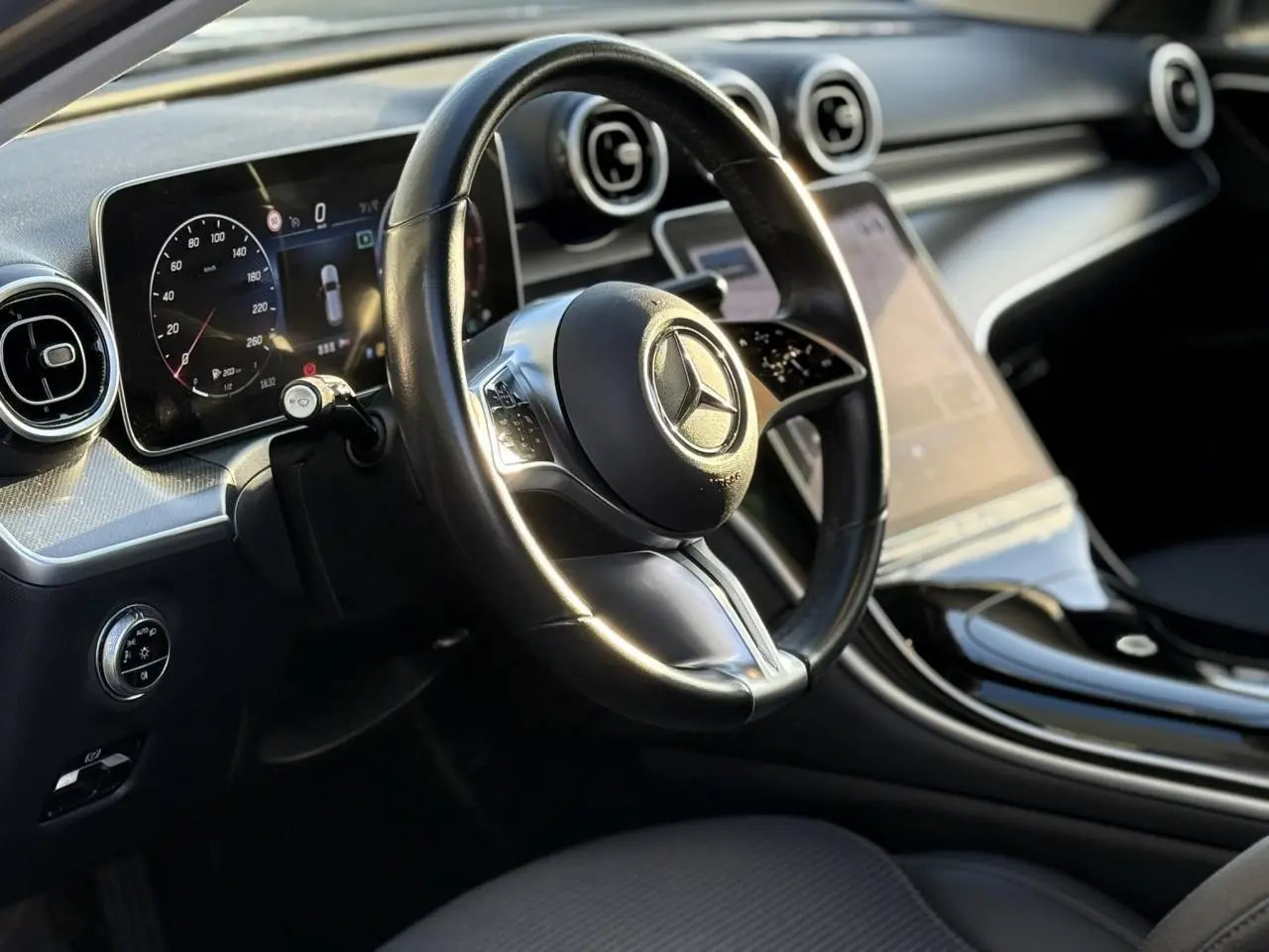 Gros plan sur le volant et la portière côté gauche d'une Mercedes Classe C Break argent avec commandes au volant et finitions noires brillantes.