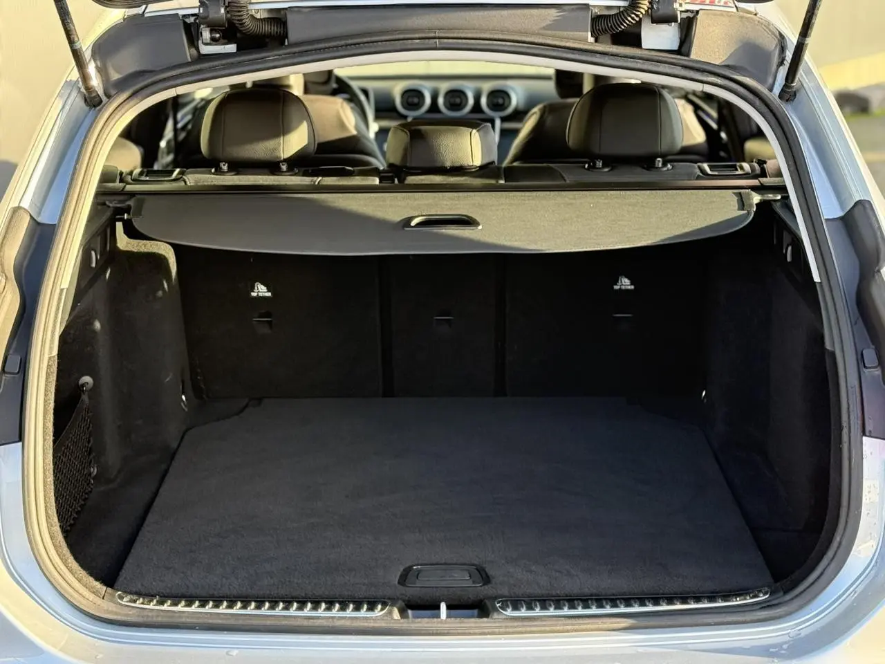 Coffre ouvert vu de l'arrière d'un Mercedes Classe C Break argent High-Tech, intérieur noir et cache-bagages déployé.