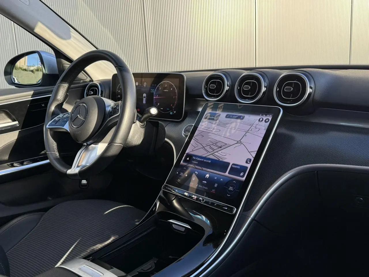 Vue intérieure avant du tableau de bord et volant Mercedes Classe C Break V 200d 2023 avec écran tactile vertical et finition noir brillant