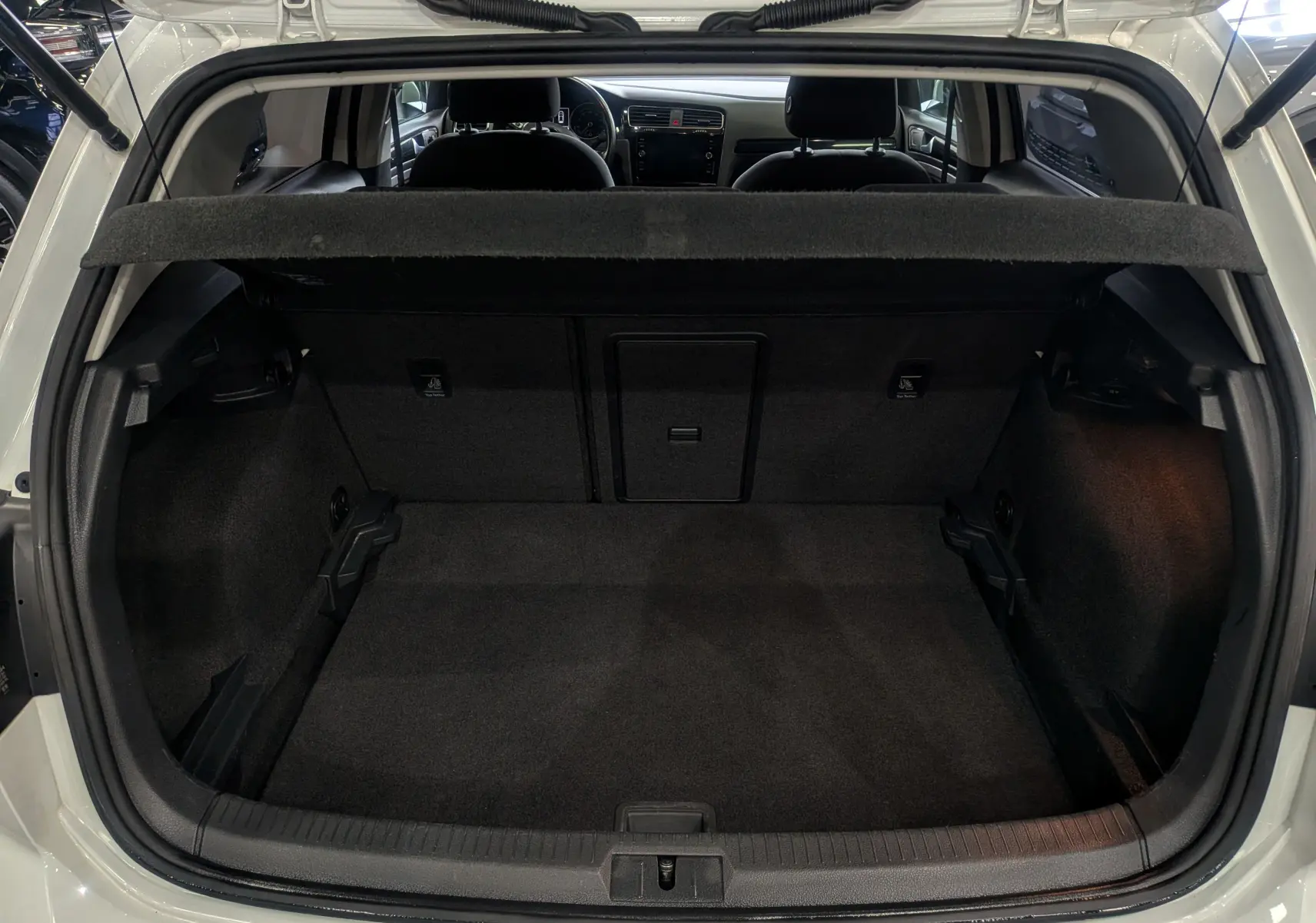 Coffre ouvert d'une Volkswagen Golf VII TSI 125 ch Sound blanc pur, vue arrière montrant l'intérieur spacieux et la banquette arrière.