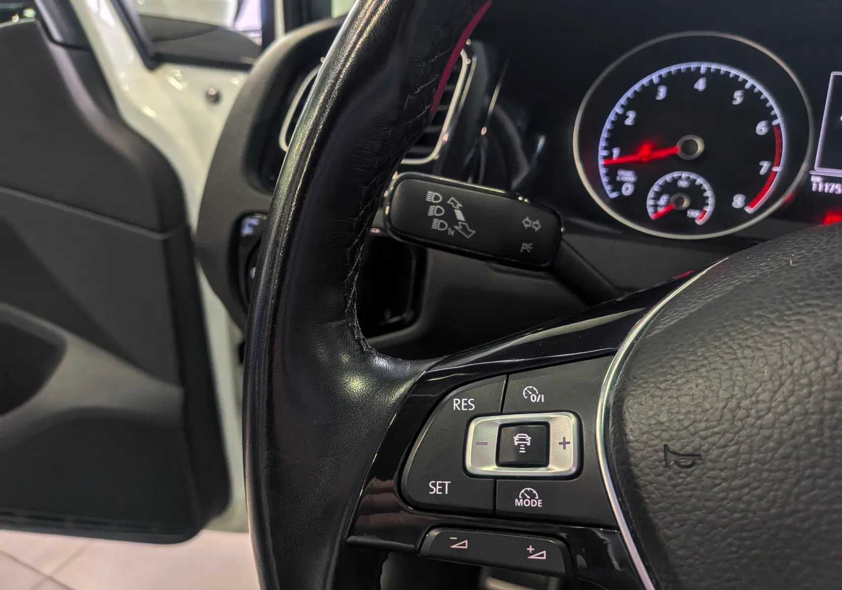 Gros plan sur le volant noir de la Volkswagen Golf VII TSI 125 CH Sound, avec tableau de bord et portière blanche en arrière-plan.