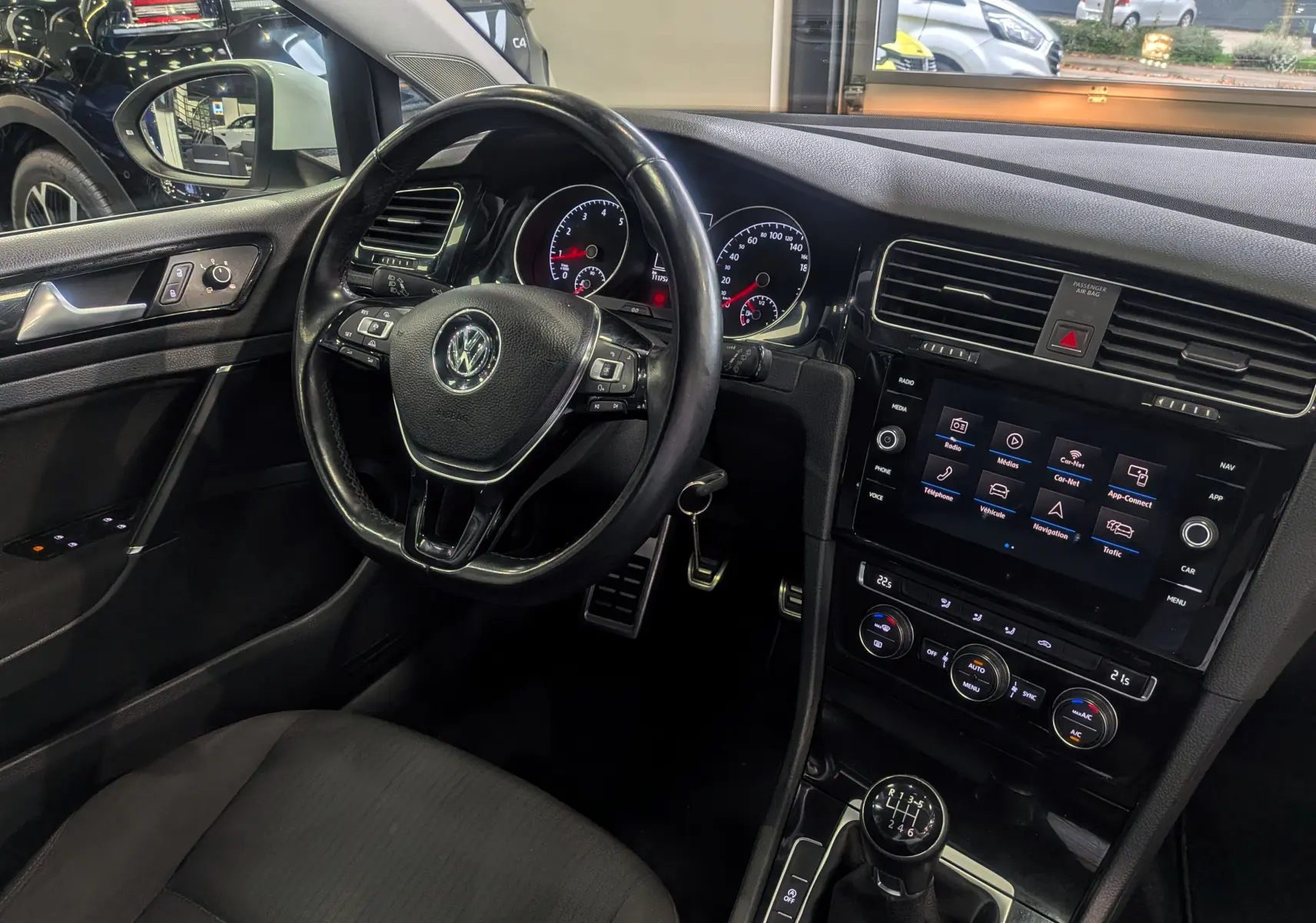 Vue intérieure côté conducteur d'une Volkswagen Golf VII blanche, avec volant multifonction et boîte manuelle six vitesses.