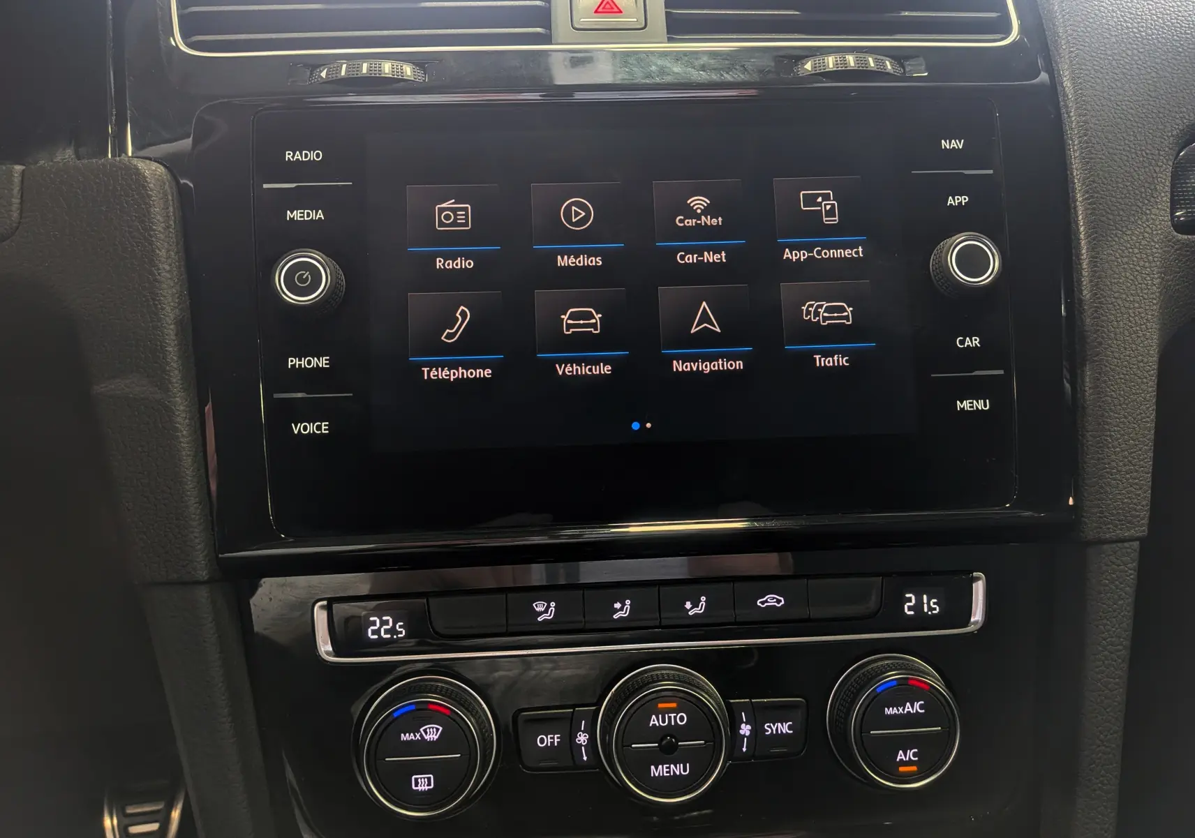 Vue rapprochée de l'écran tactile et de la console de climatisation d'une Volkswagen Golf VII blanche, intérieur noir.