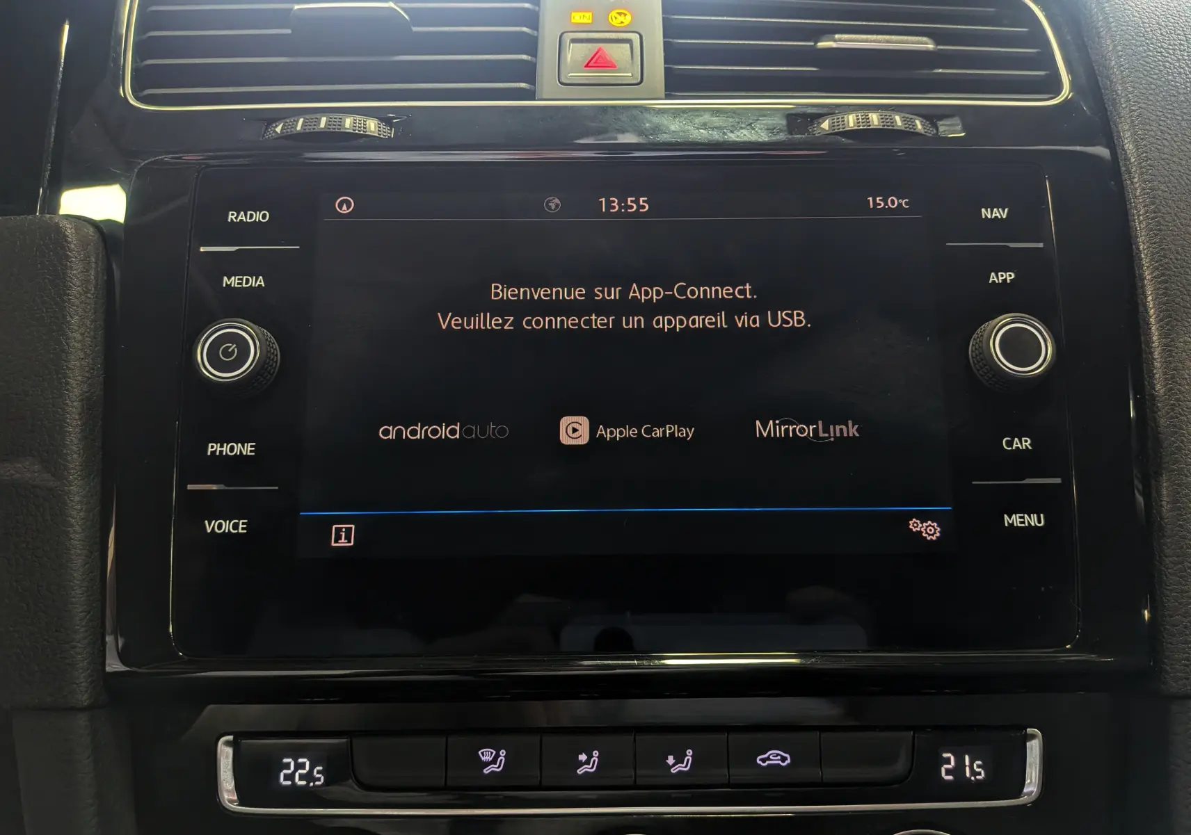 Vue rapprochée de l'écran tactile central noir du Volkswagen Golf VII blanc, affichant App-Connect et commandes climatisation.