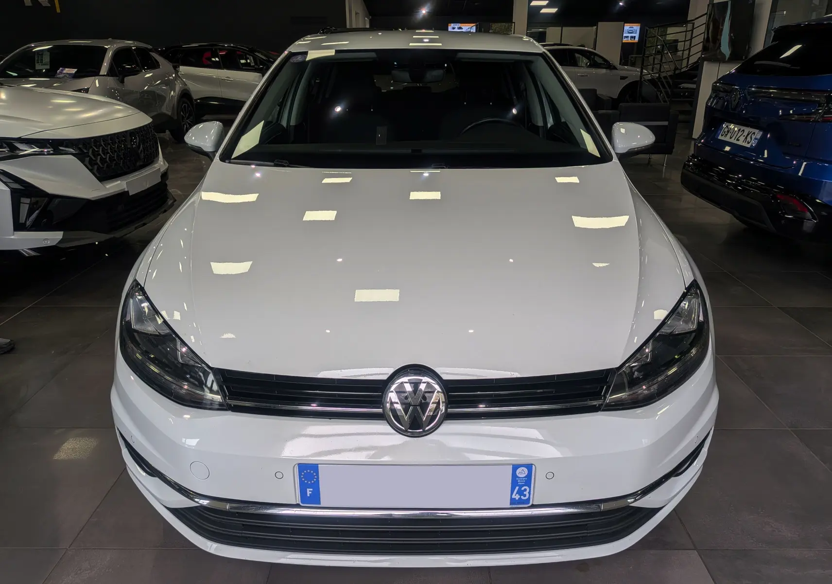 Vue avant d'une Volkswagen Golf VII TSI 125 CH Sound blanche Pure exposée en showroom avec éclairage intérieur.