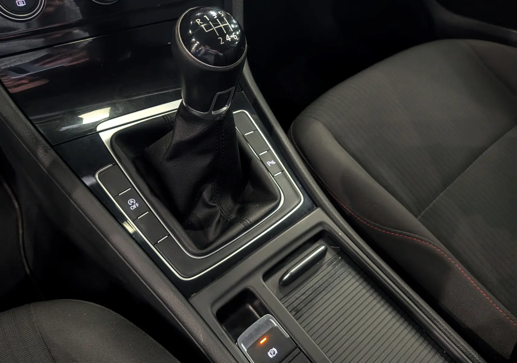 Gros plan sur la console centrale de la Volkswagen Golf VII TSI 125 CH Sound avec levier de vitesse manuel et sièges tissu noirs.