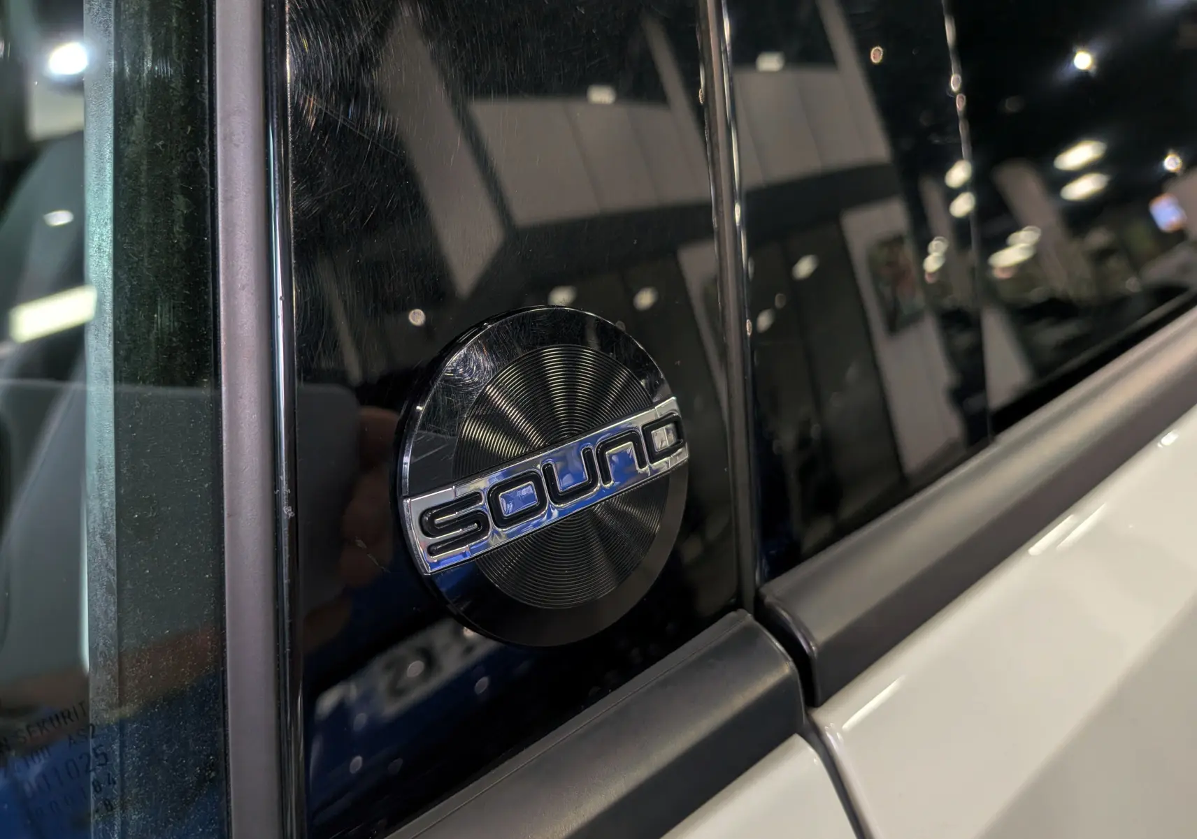 Gros plan sur l'écusson "Sound" noir et argent sur la porte blanche côté gauche d'une Volkswagen Golf VII.