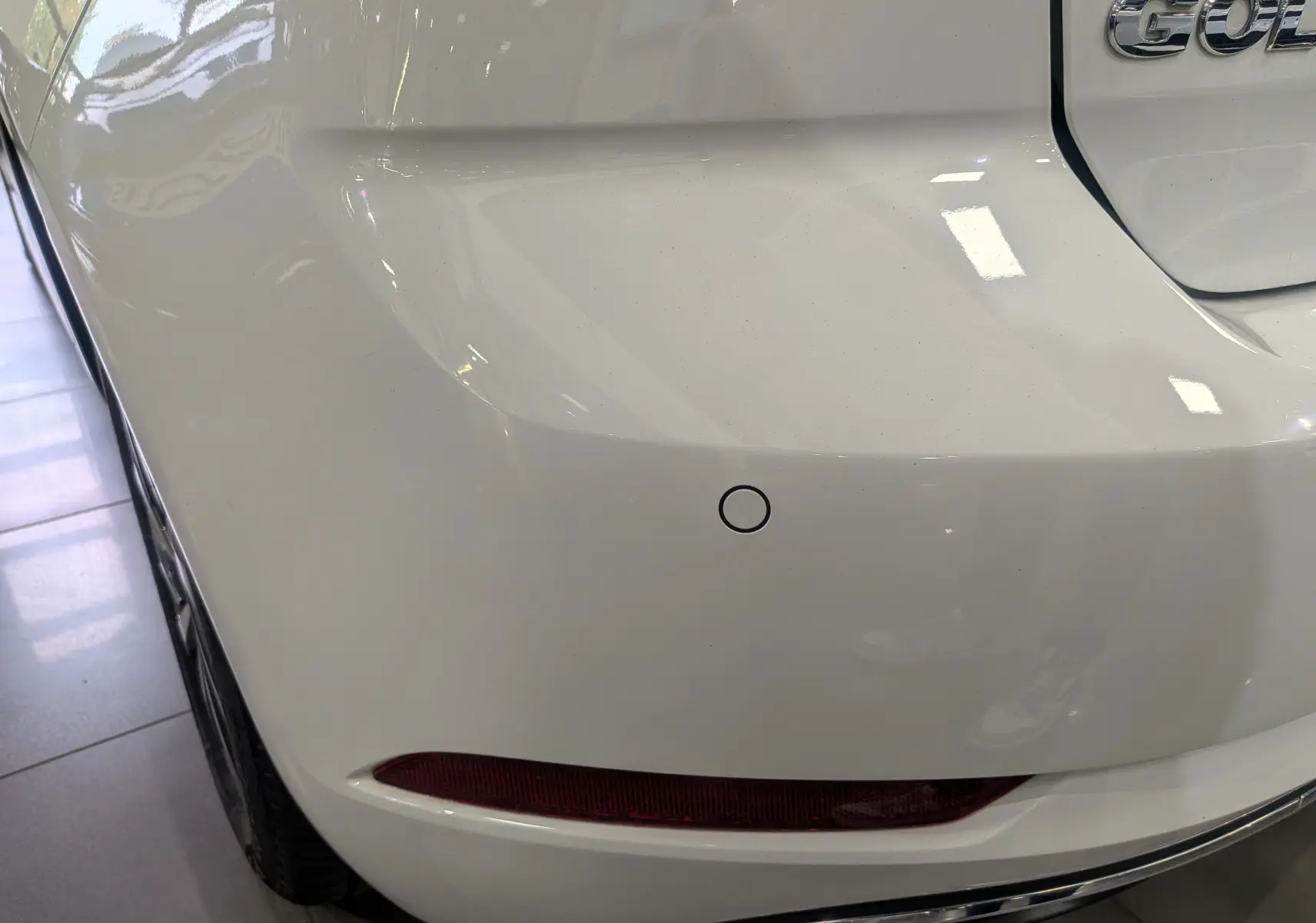 Gros plan sur l'angle arrière gauche d'une Volkswagen Golf VII TSI blanche, avec feu arrière et capteur de recul visibles.