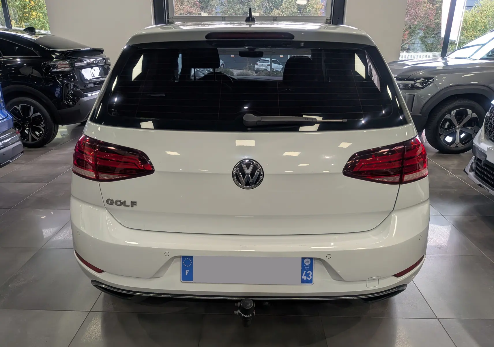 Vue arrière d'une Volkswagen Golf VII blanche avec logo et feux rouges, stationnée en intérieur showroom.