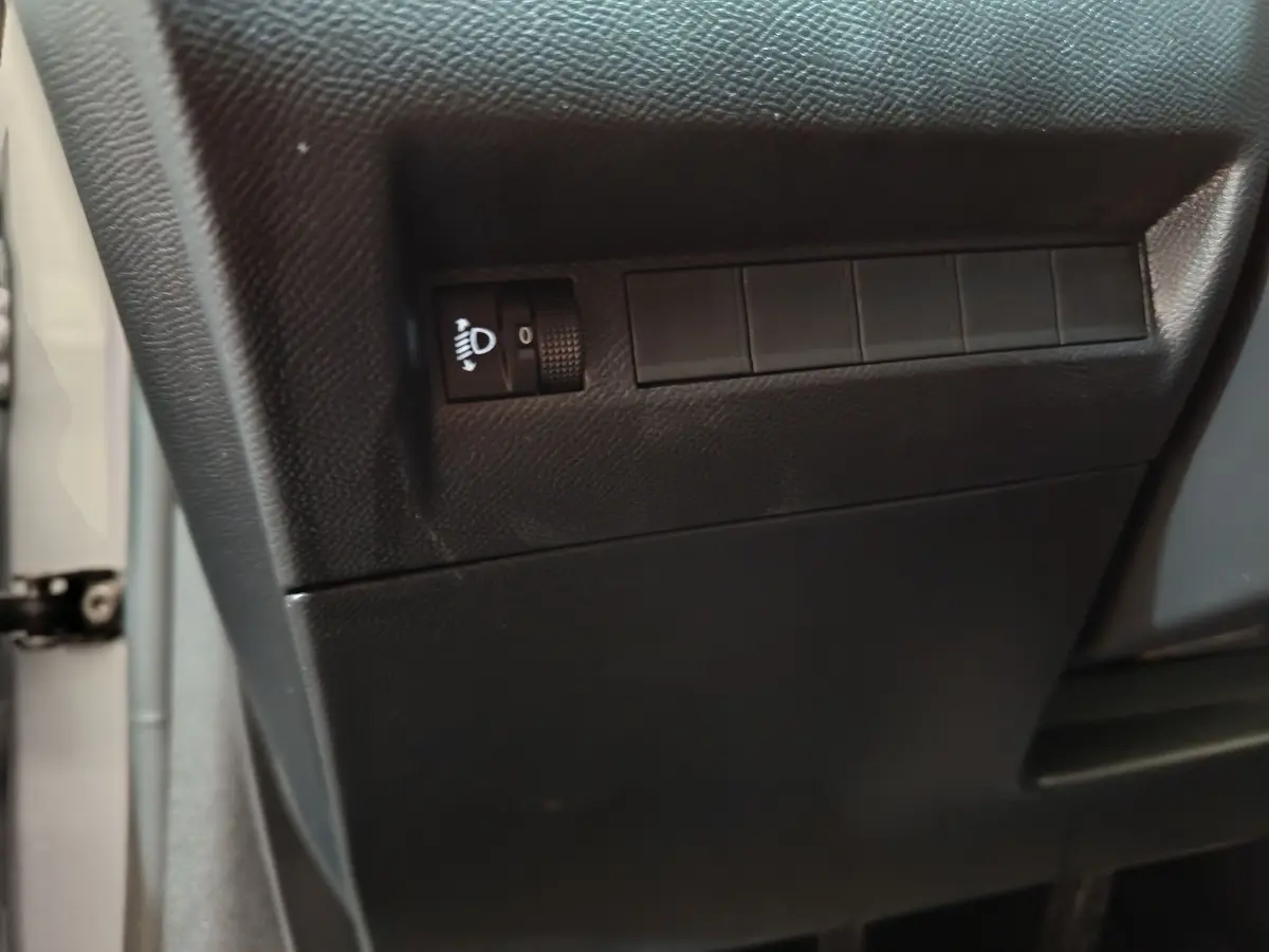 Détail du tableau de bord côté conducteur de la Peugeot 208 gris clair montrant la molette de réglage des phares.
