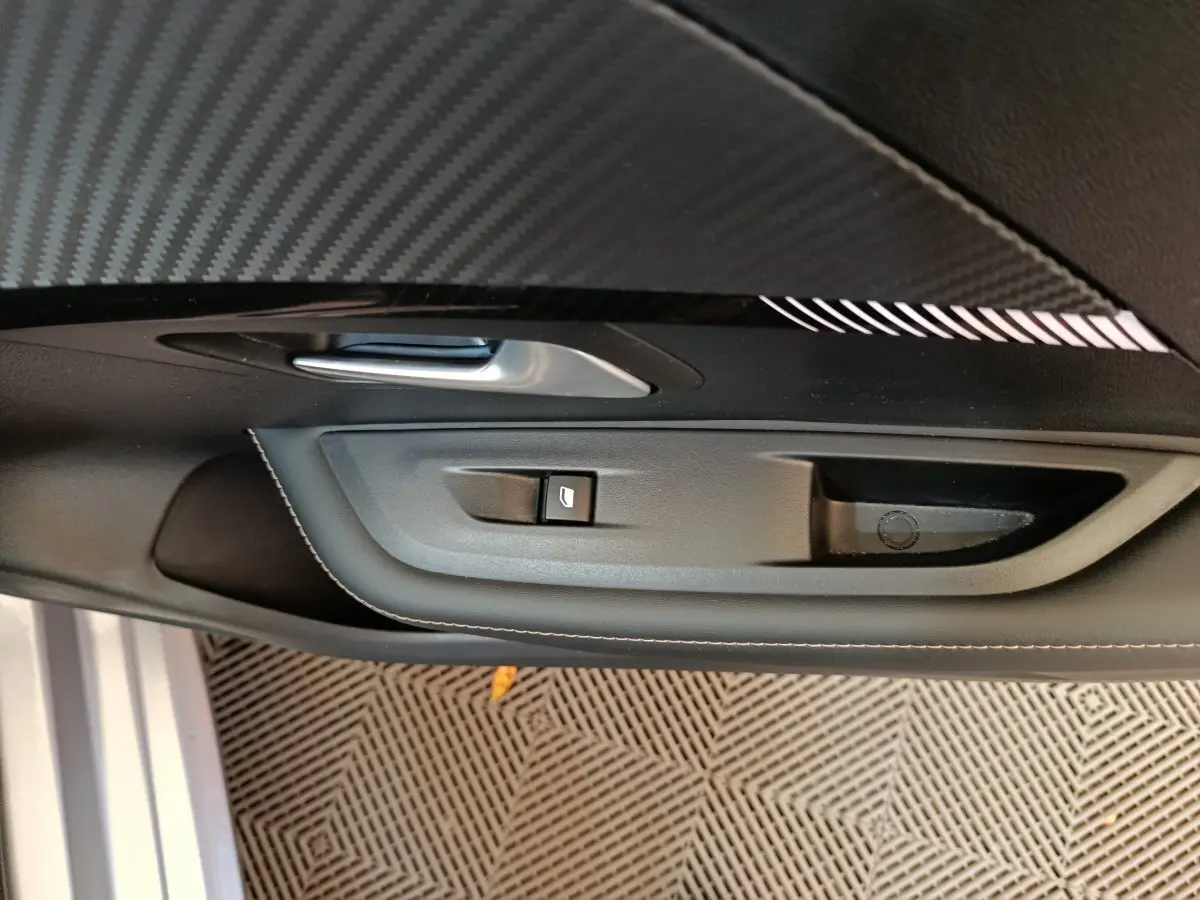 Poignée intérieure et commande de lève-vitre côté gauche de la porte d'une Peugeot 208 gris clair, finition Allure.