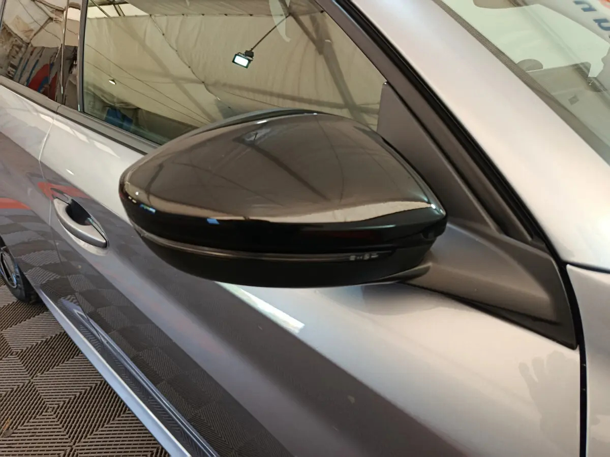 Rétroviseur noir brillant côté conducteur sur Peugeot 208 gris clair, vue rapprochée du profil avant gauche.