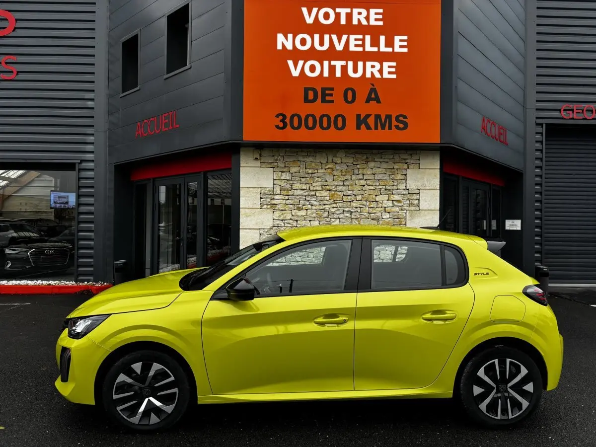 Peugeot 208 Hybrid jaune vue de profil côté gauche, avec jantes noires et toit noir, devant un bâtiment commercial.