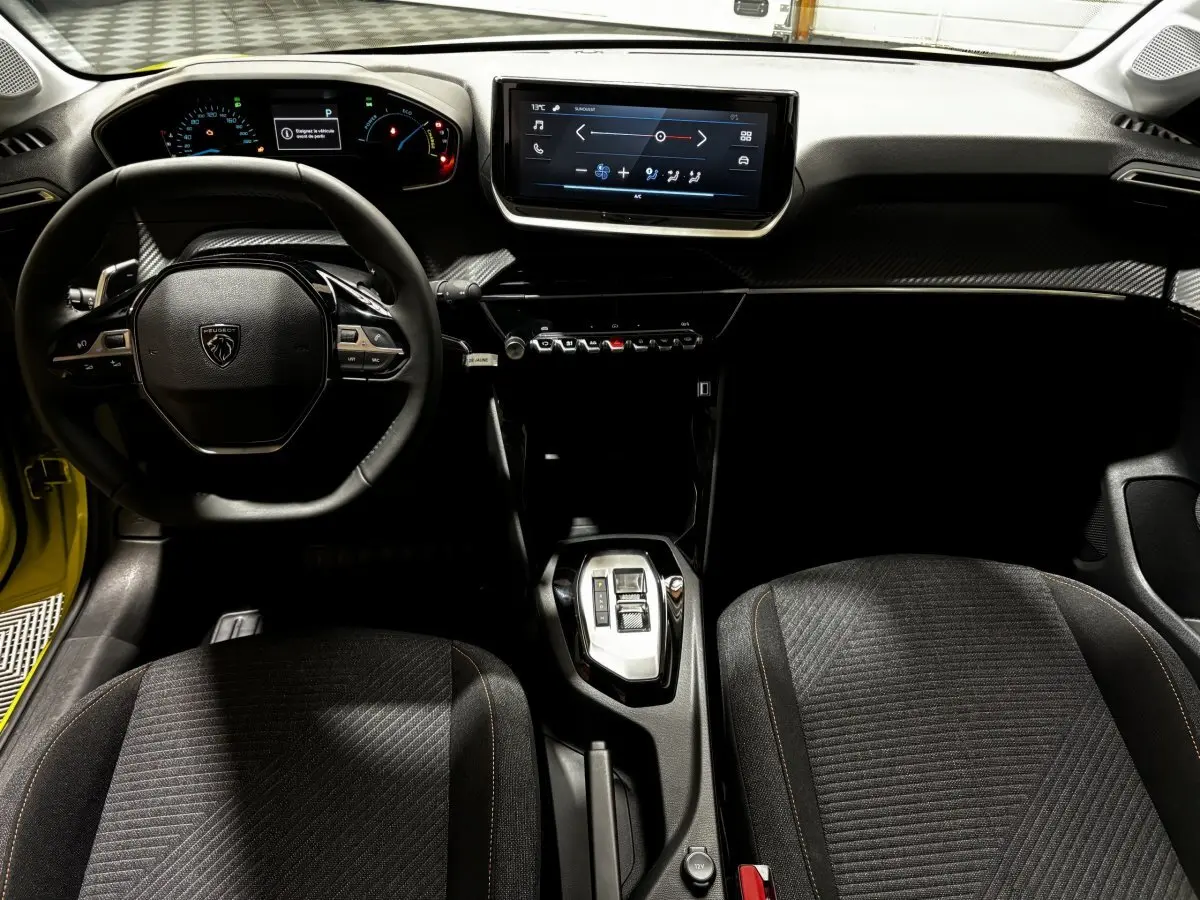 Vue intérieure avant de la Peugeot 208 Hybrid jaune, montrant le volant cuir multifonctions et l'écran tactile central.
