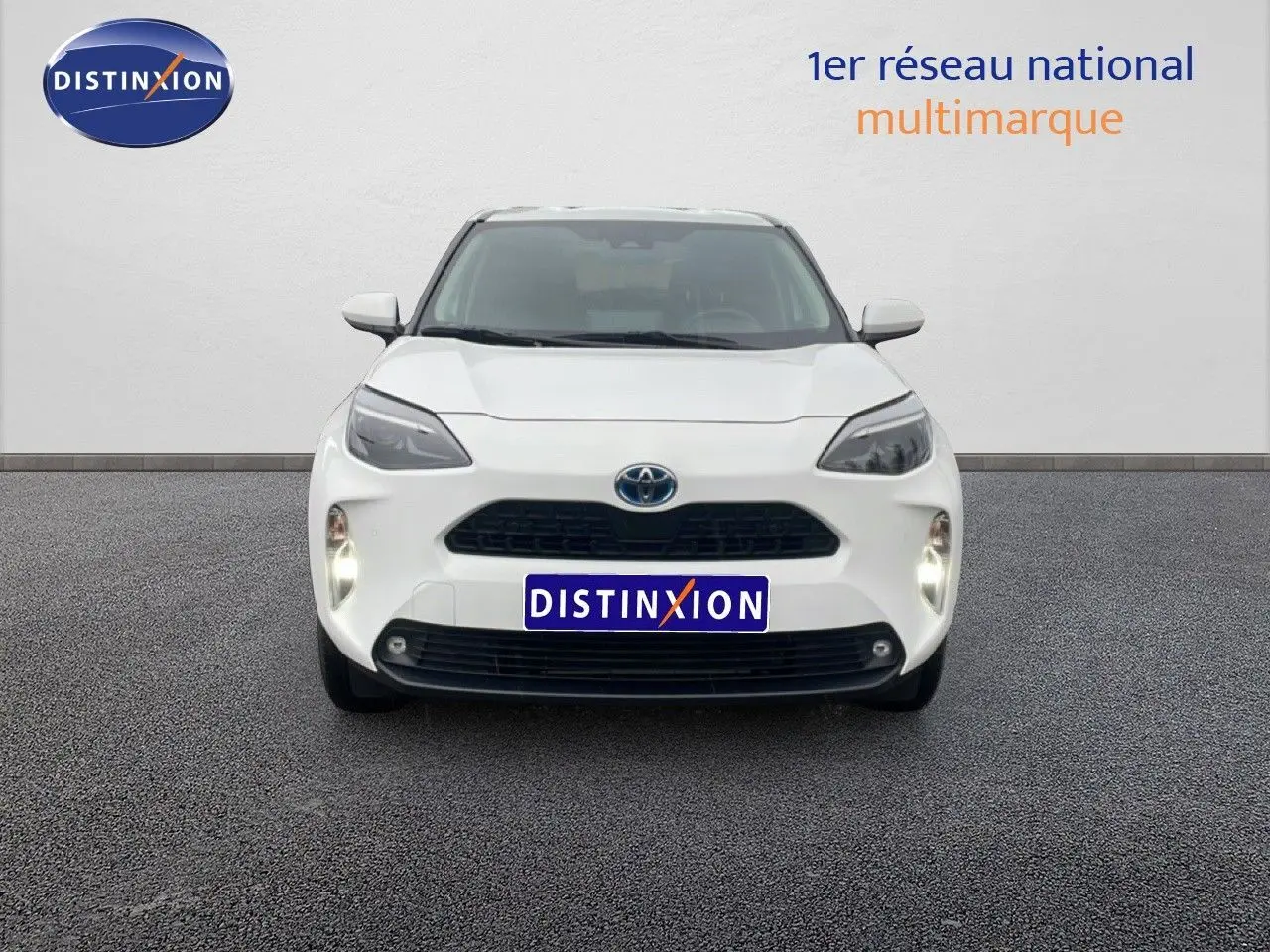 Vue frontale d'une Toyota Yaris Cross Hybrid blanche 2024 avec phares allumés sur fond neutre.