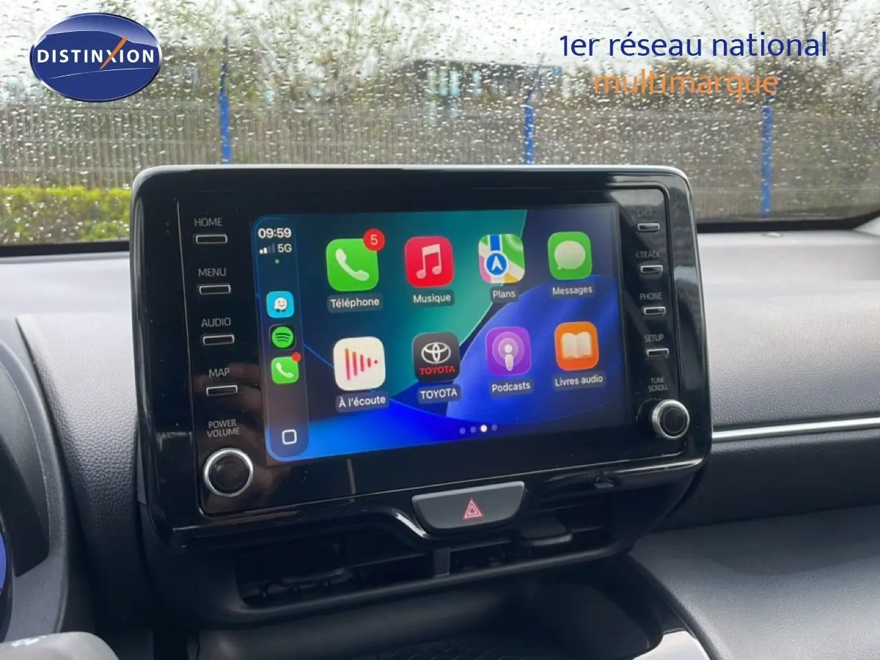 Écran tactile central allumé dans l’habitacle d’une Toyota Yaris Cross blanche, vue de face sous la pluie.