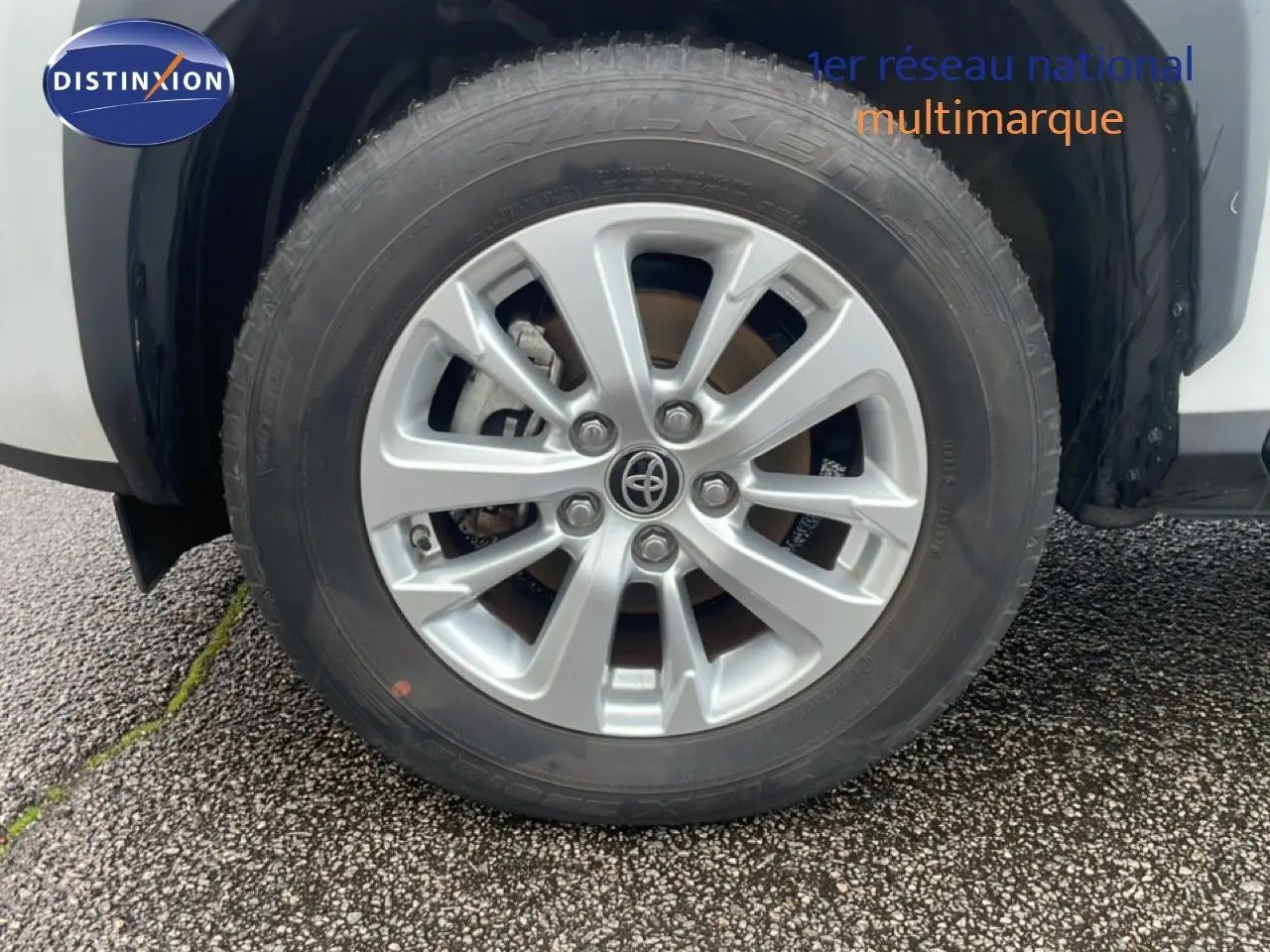 Gros plan sur la roue avant droite avec jante alliage argentée du Toyota Yaris Cross blanc hybride 2024.