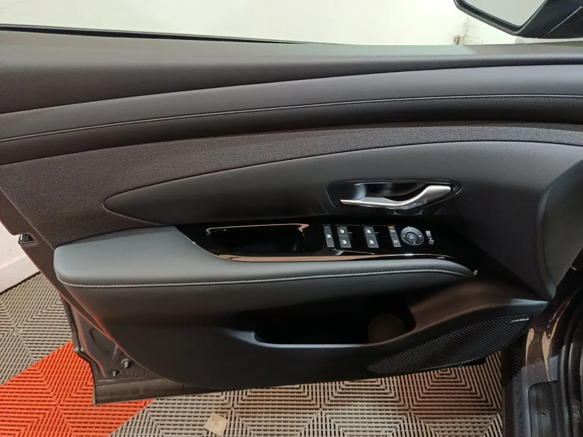 Intérieur côté conducteur de la porte d’un Hyundai Tucson gris foncé, avec commandes électriques et poignée argentée.