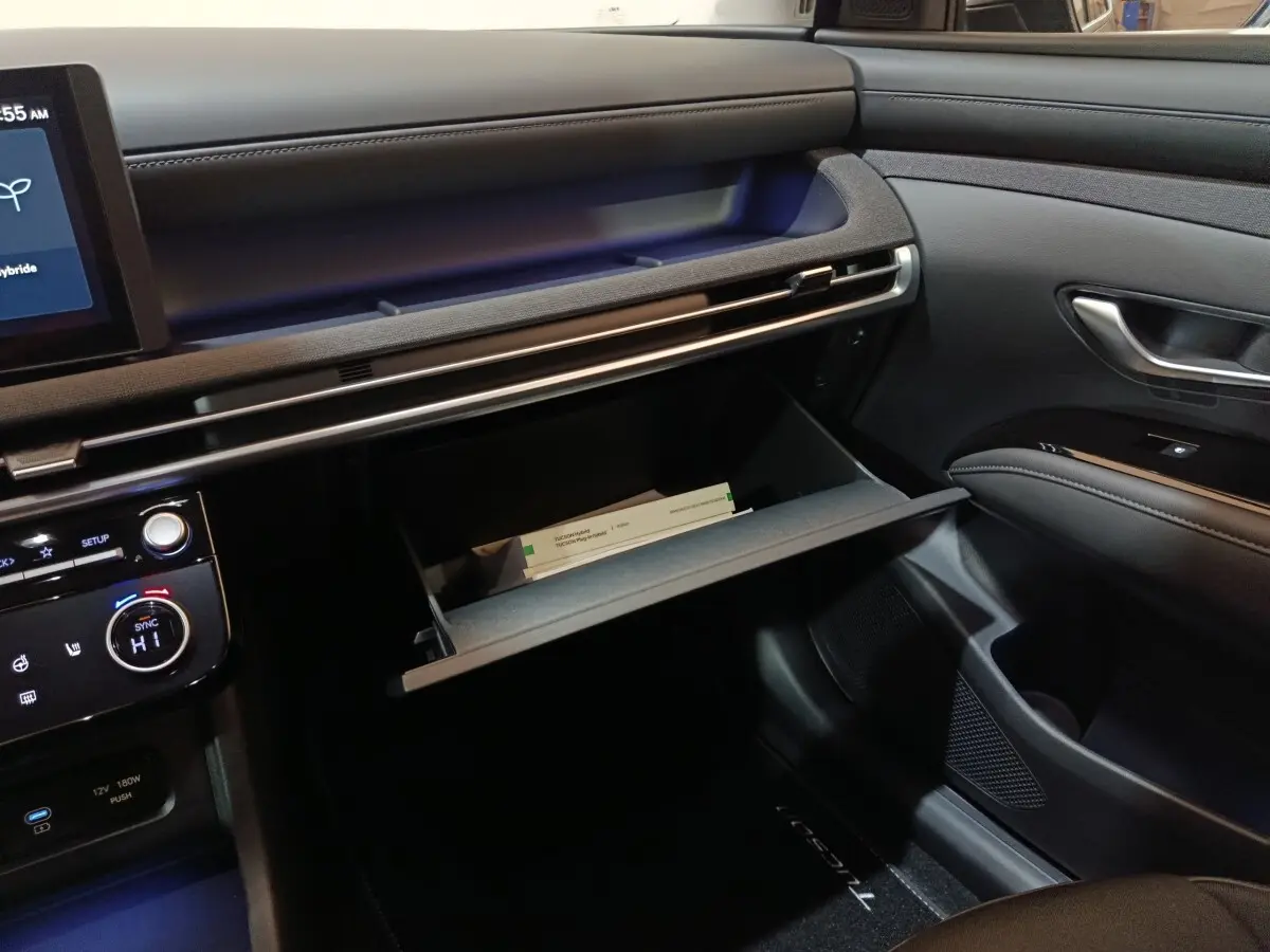 Intérieur du Hyundai Tucson 2025 gris foncé, vue côté passager sur la boîte à gants ouverte et tableau de bord moderne.