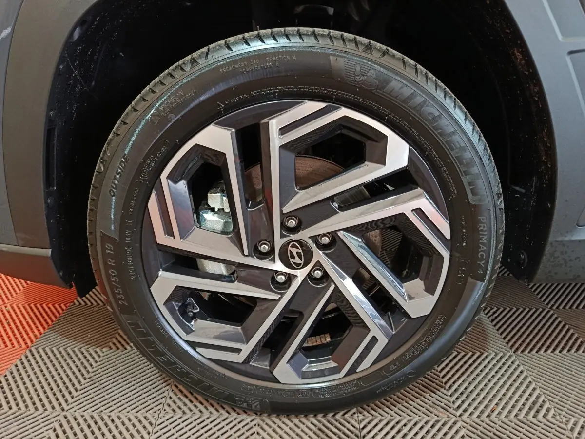 Gros plan sur la roue avant gauche du Hyundai Tucson gris foncé, mettant en valeur la jante alliage au design géométrique.