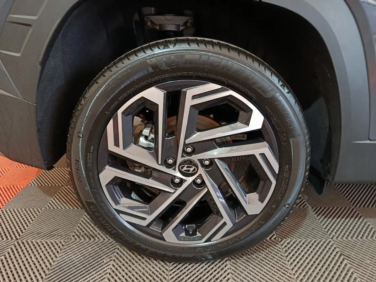 Gros plan sur la roue avant droite du Hyundai Tucson gris foncé, mettant en valeur la jante alliage au design géométrique.