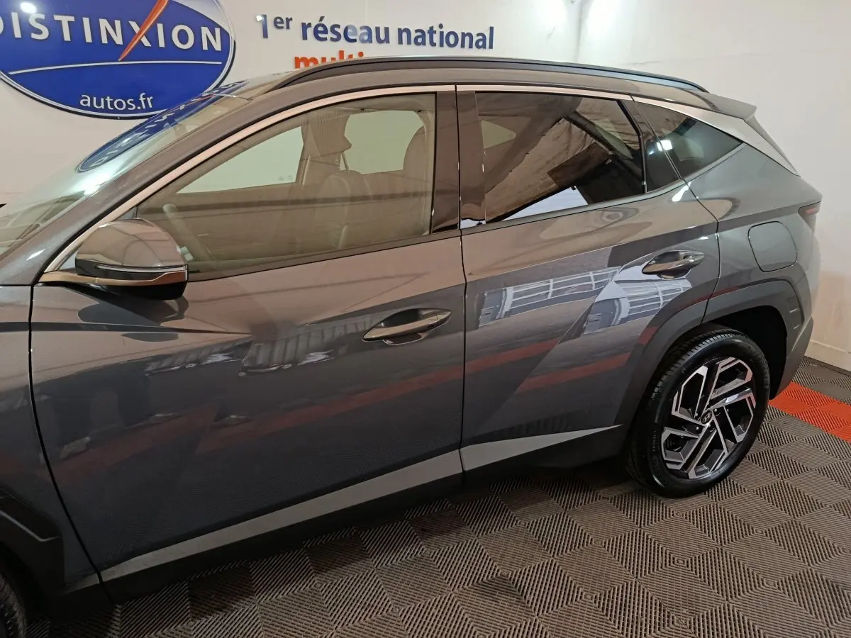 Vue de profil côté gauche du Hyundai Tucson 1.6 Hybrid gris foncé, mettant en valeur ses jantes modernes et ses lignes anguleuses.