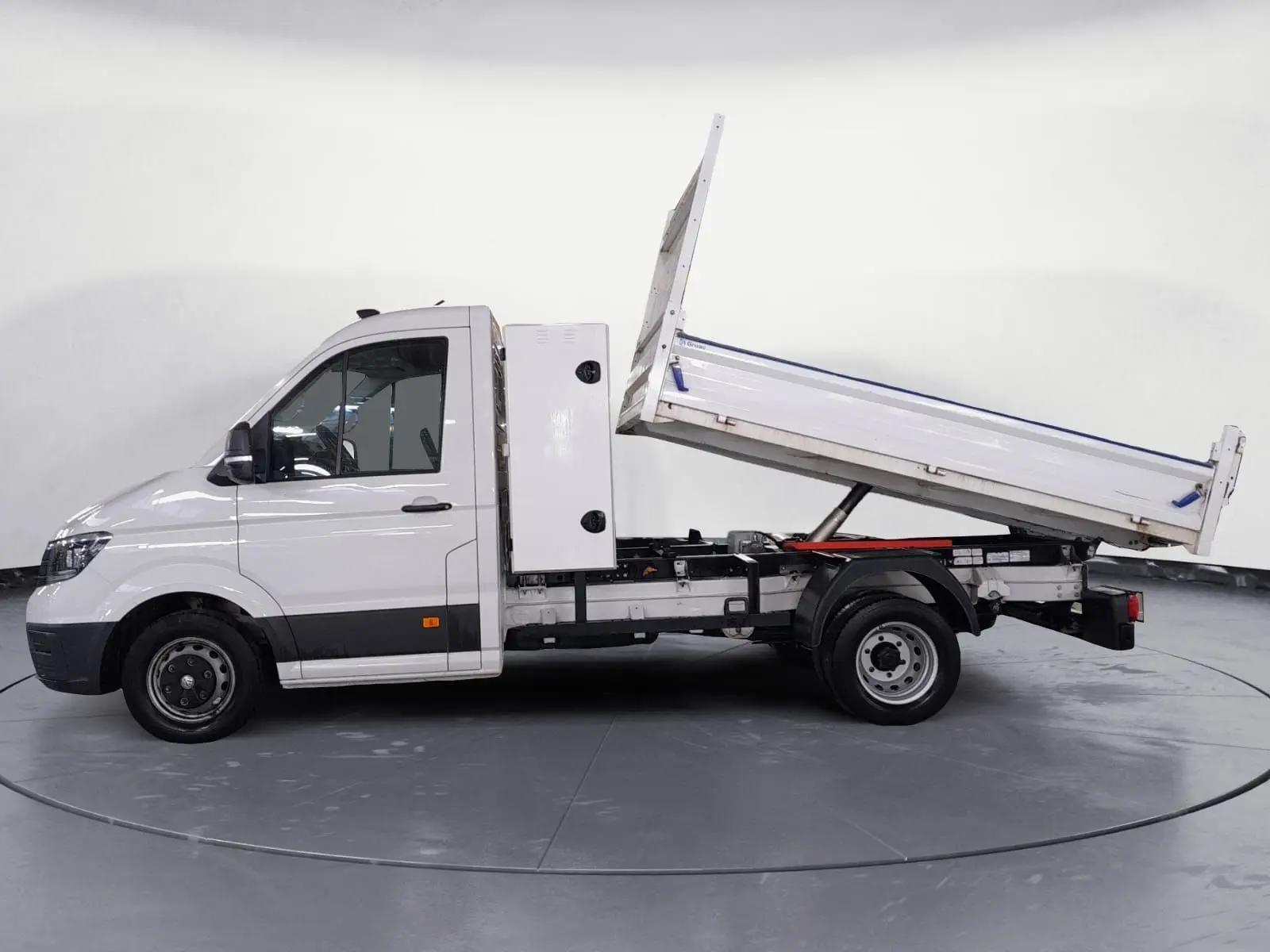 Vue latérale droite d’un Volkswagen Crafter blanc avec benne relevée et coffre latéral, roues jumelées visibles.