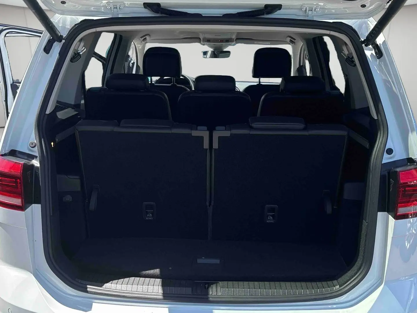 Vue arrière du Volkswagen Touran blanc avec hayon ouvert montrant les sièges arrière et le coffre fermé.