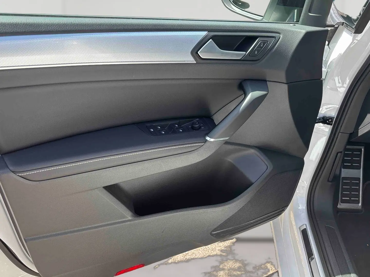 Vue intérieure de la porte avant gauche du Volkswagen Touran blanc, avec commandes de vitres et poignée argentée.