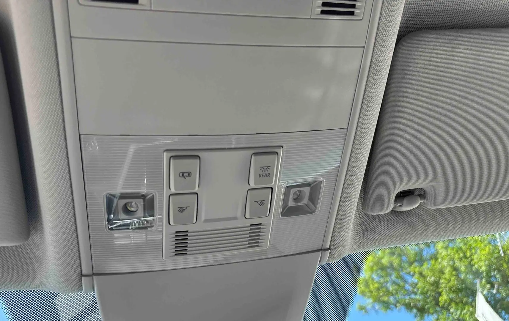 Plafonnier intérieur gris clair avec commandes d’éclairage et pare-soleil partiel du Volkswagen Touran blanc, vue de dessous.