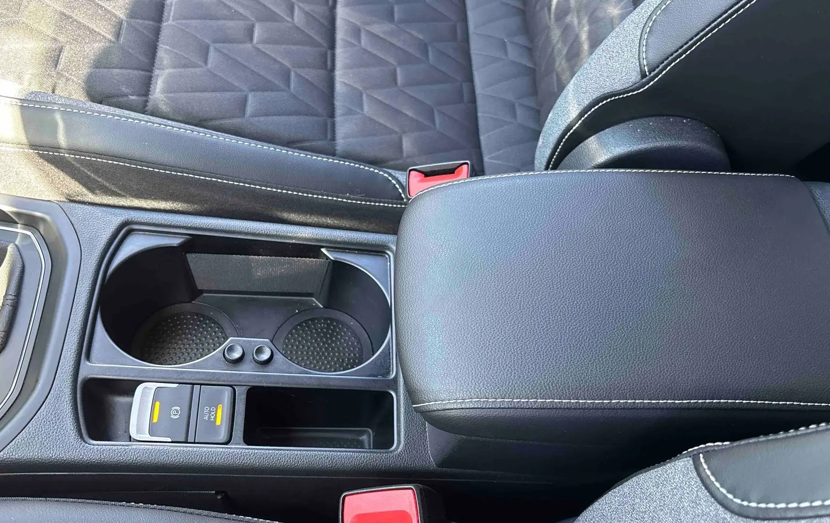 Vue rapprochée de la console centrale noire du Volkswagen Touran 2025 avec accoudoir et porte-gobelets.