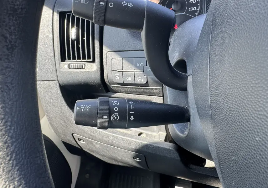 Gros plan sur les commandes au volant et la ventilation du tableau de bord noir du Peugeot Boxer Fourgon blanc 2019.