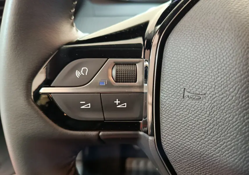 Gros plan sur les commandes gauche du volant cuir de la Peugeot 208 PureTech 100 S&S Allure 2025 gris clair