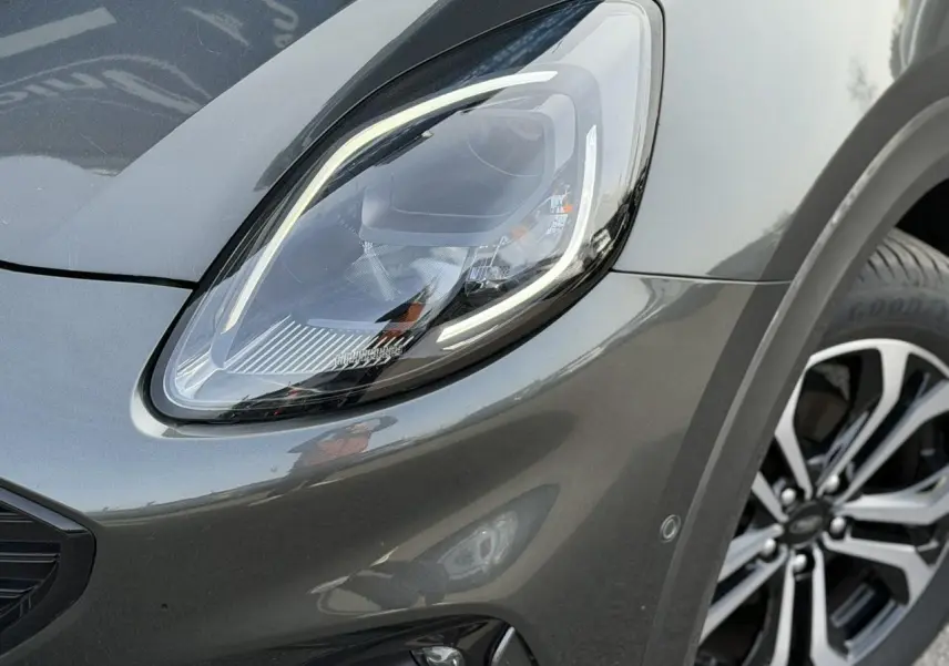 Gros plan sur le phare avant gauche et la roue alliage 17 pouces du Ford Puma gris magnétique 2024.