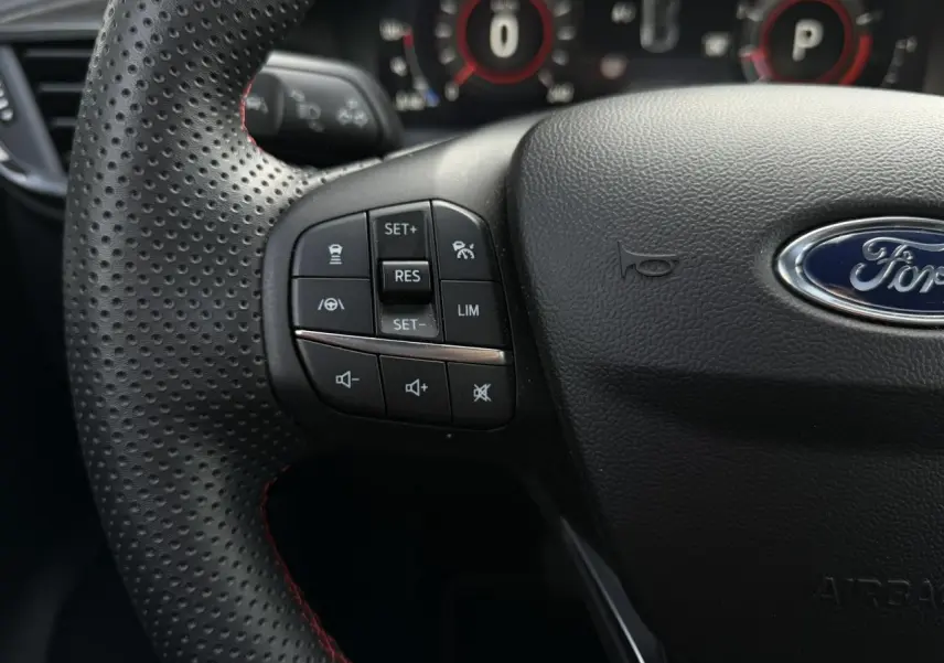 Gros plan sur le volant perforé noir ST-Line du Ford Puma 2024 avec commandes intégrées et logo Ford central.