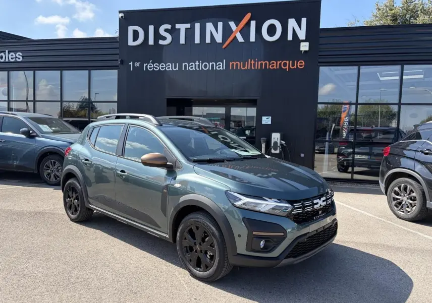 Vue 3/4 avant droite d'une Dacia Sandero III Stepway Vert Cèdre avec jantes noires et rétroviseurs cuivrés, devant un showroom Distinxion.