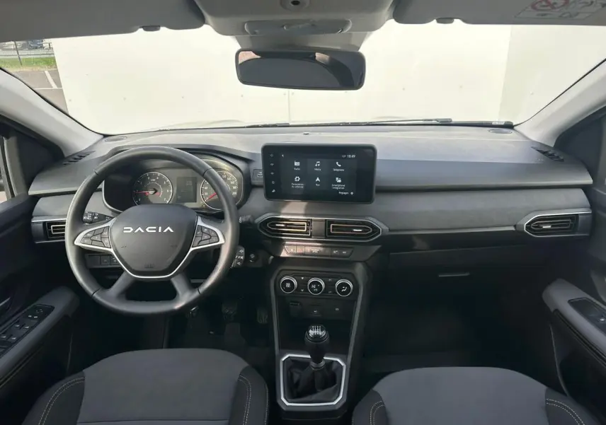 Vue intérieure avant du tableau de bord et volant de la Dacia Sandero III Stepway avec écran tactile et boîte manuelle.