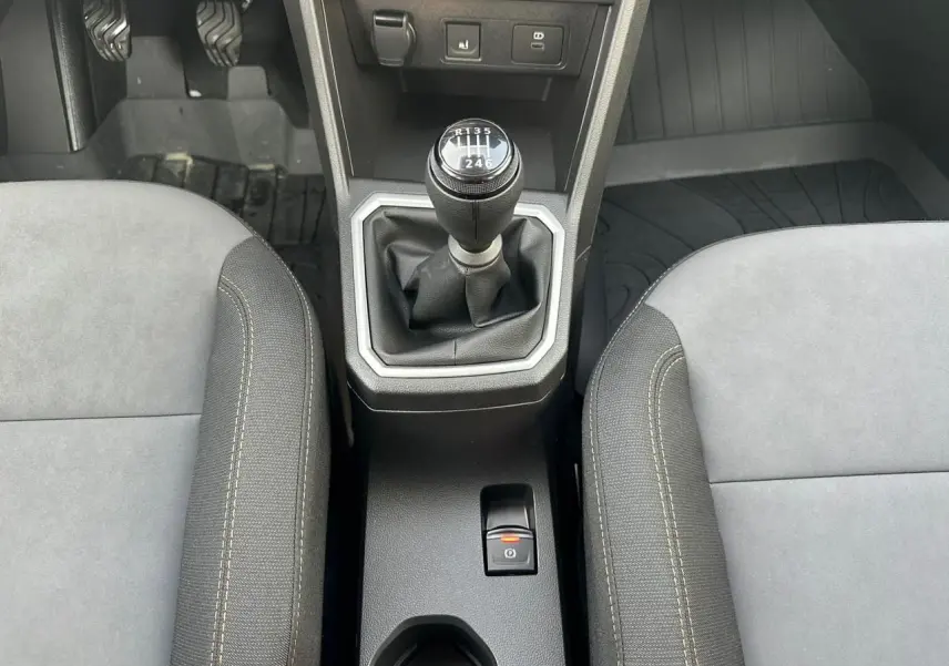 Vue rapprochée de la console centrale intérieure de la Dacia Sandero III Stepway, avec levier de vitesses manuel et frein de parking électrique.